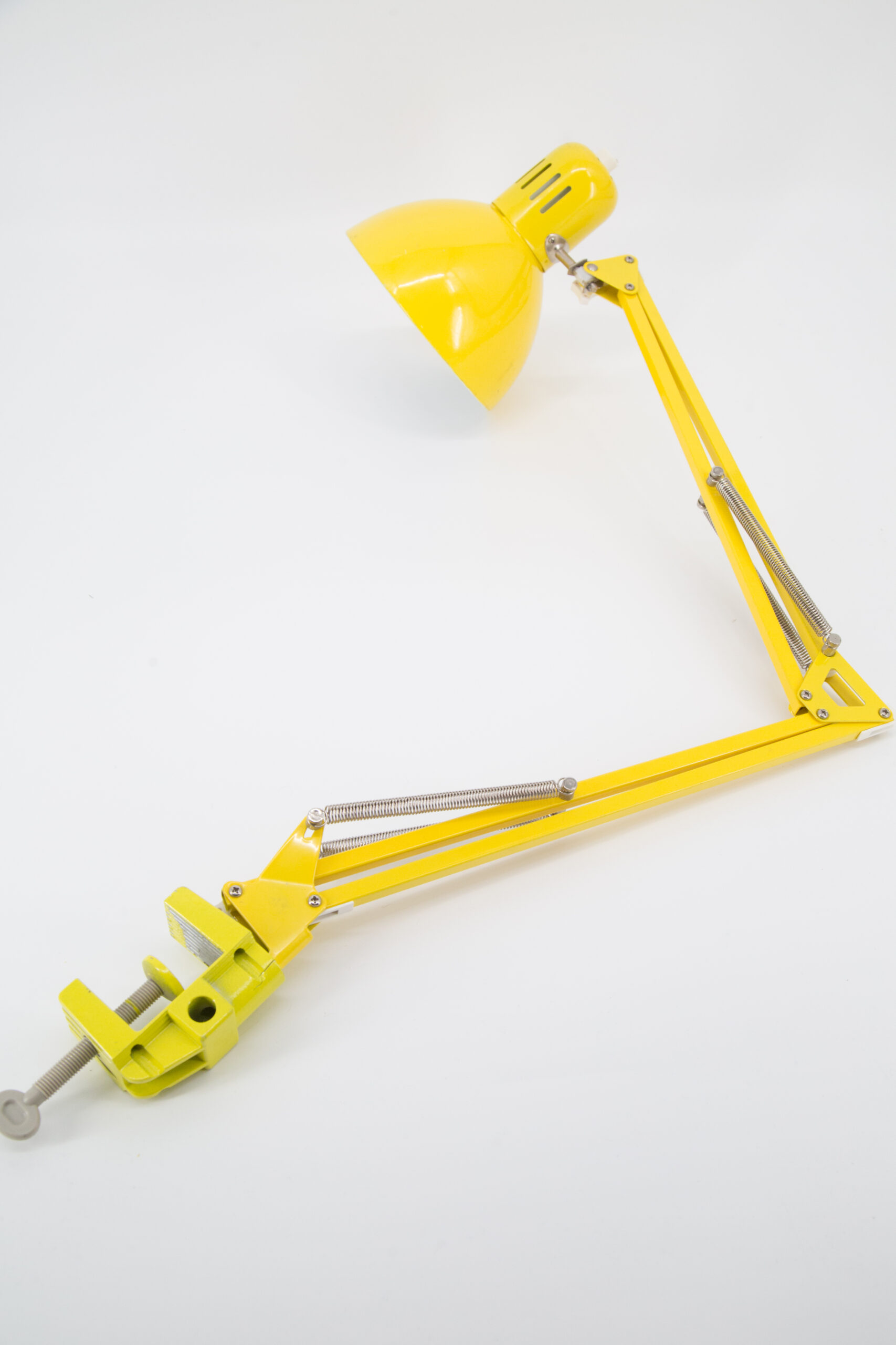 Lampada da tavolo gialla brillante con braccio articolato esteso e base a morsetto, su sfondo bianco.