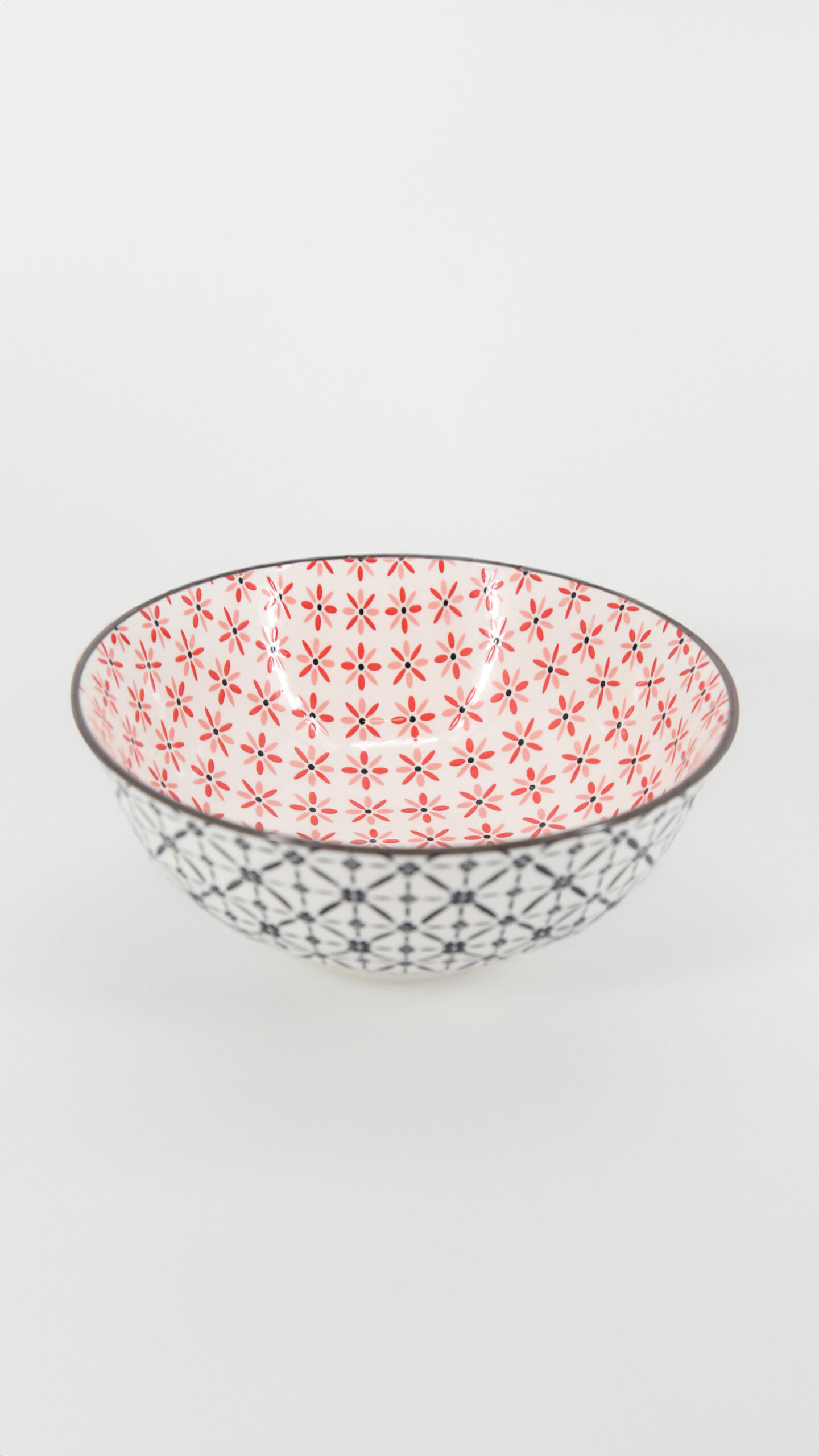 Ciotola in ceramica bianca con interno a fiori rossi e rosa e esterno a pattern geometrico nero, su sfondo bianco.
