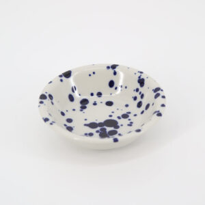 Ciotola in ceramica bianca con macchie blu scuro irregolari, vista dall'alto su sfondo bianco.