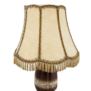 Lampada da tavolo vintage con base in ceramica marrone e paralume in tessuto beige con frange e trecce decorative, su sfondo bianco.