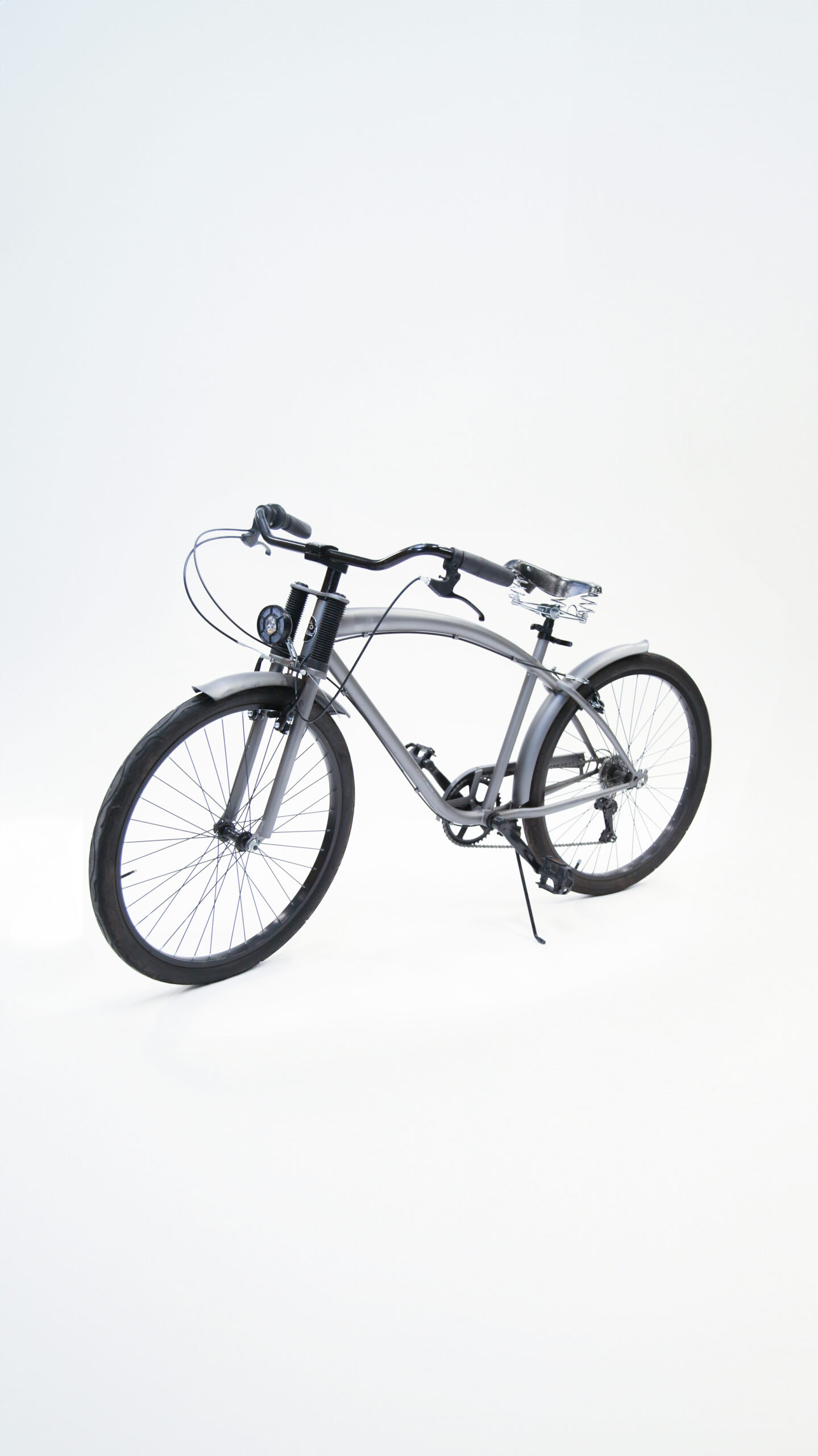 Bicicletta cruiser grigia con telaio curvo, manubrio ampio, sella ammortizzata e parafanghi, vista laterale su sfondo bianco.