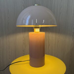 Lampada da tavolo con paralume a cupola grigio e interno giallo, base cilindrica con sfumatura arancione-marrone, su un tavolo giallo.
