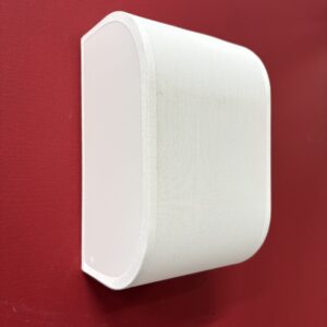 Diffusore audio da parete bianco con lati curvi in tessuto, montato su una parete rossa, ideale come oggetto di scena.