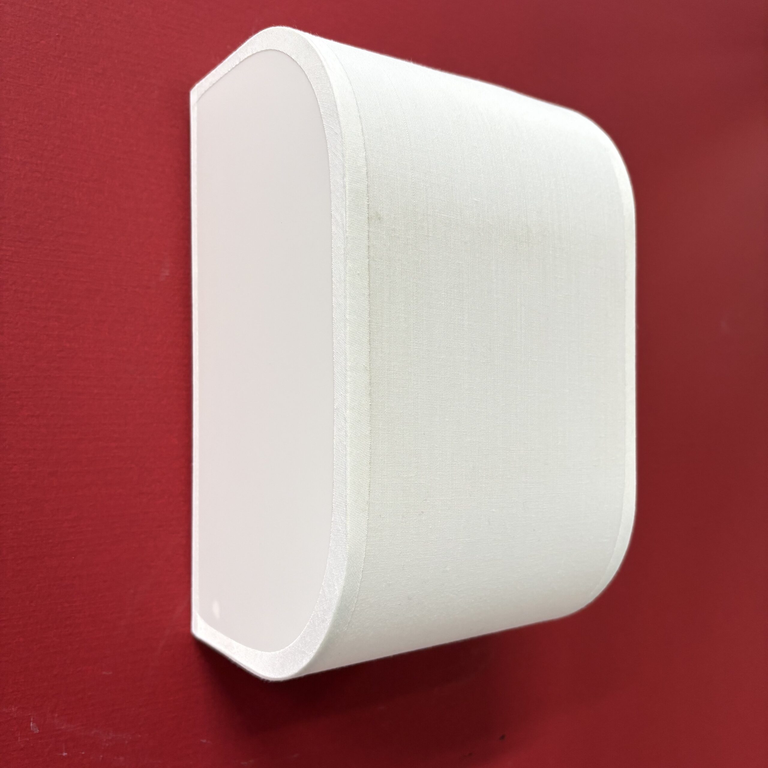 Diffusore audio da parete bianco con lati curvi in tessuto, montato su una parete rossa, ideale come oggetto di scena.