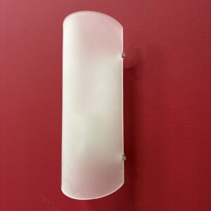 Applique murale semicilindrica con diffusore in vetro satinato bianco, montata su una parete rossa.