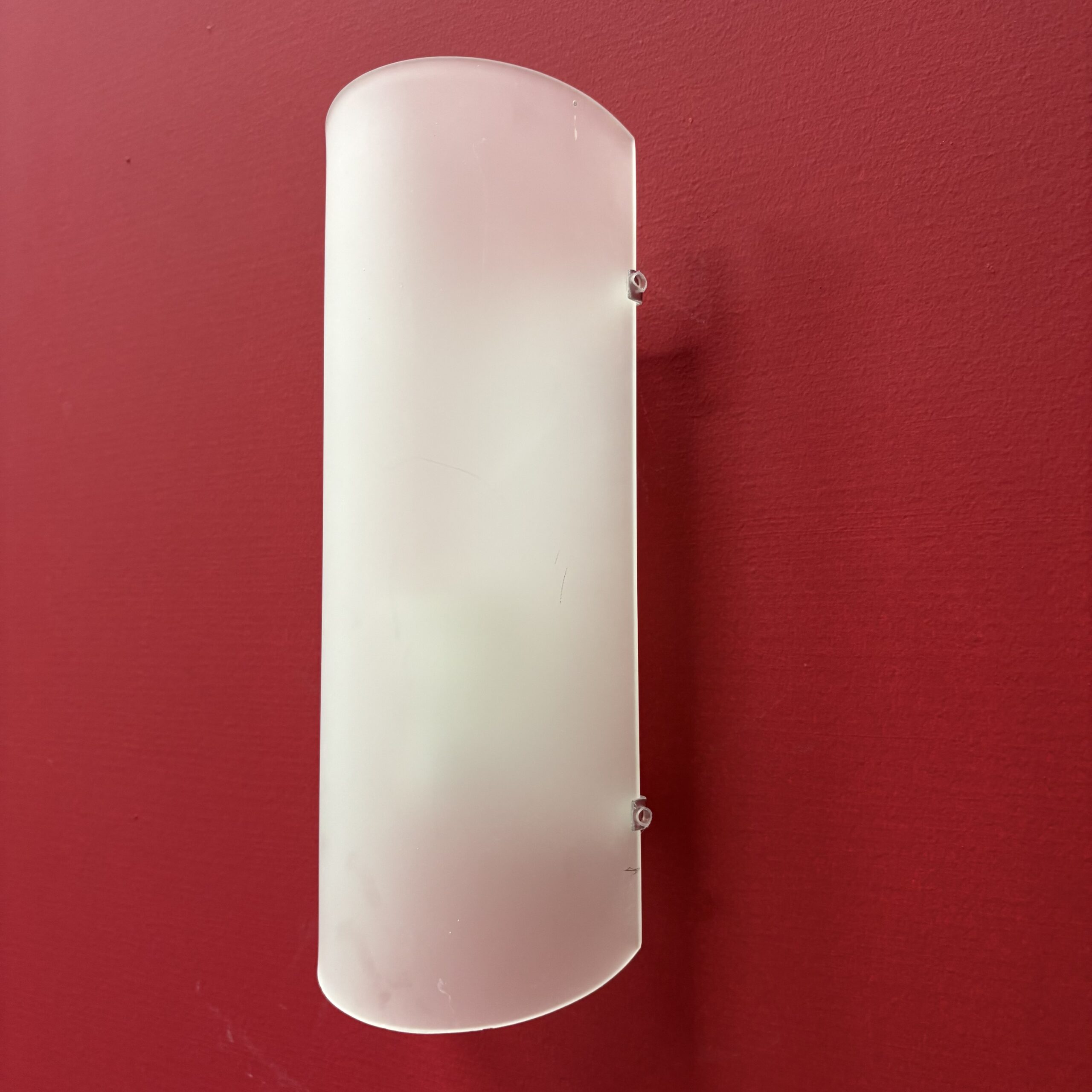 Applique murale semicilindrica con diffusore in vetro satinato bianco, montata su una parete rossa.