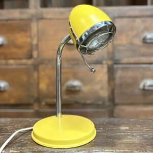 Lampada da tavolo vintage gialla con braccio flessibile cromato e base rotonda, posta su un tavolo di legno scuro.