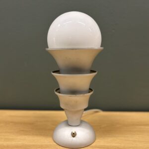 Lampada da tavolo vintage con base circolare, fusto a tre elementi conici sovrapposti e sfera luminosa opaca, su tavolo in legno.