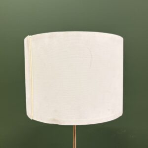 Lampada da terra con paralume cilindrico in tessuto color crema su asta metallica, sfondo verde scuro.