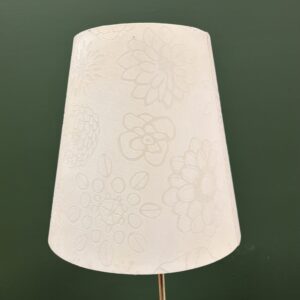 Paralume conico bianco crema con motivo floreale goffrato, su sfondo verde scuro, per noleggio scenografie.