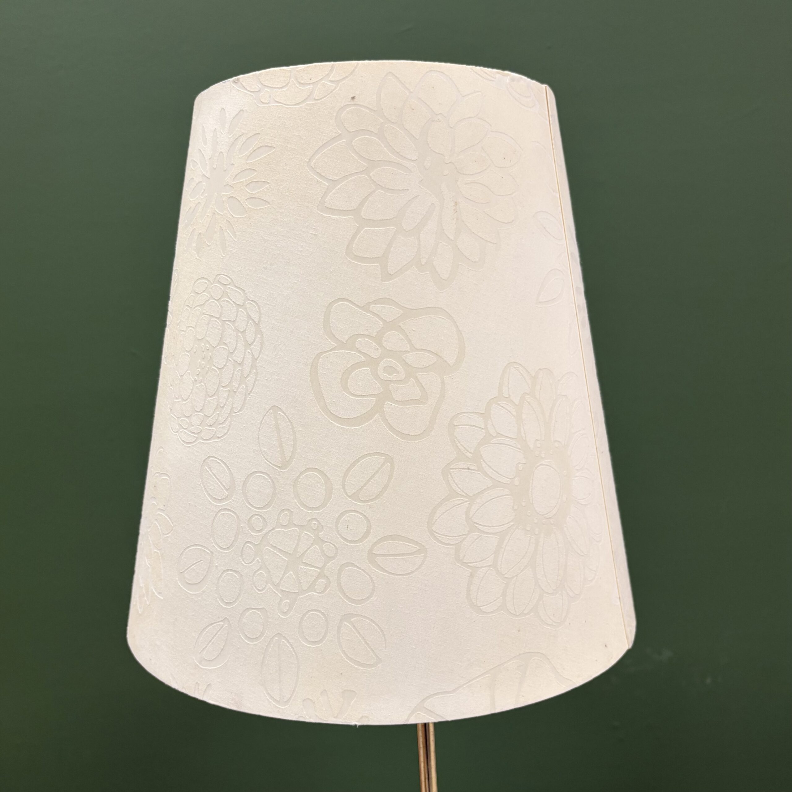 Paralume conico bianco crema con motivo floreale goffrato, su sfondo verde scuro, per noleggio scenografie.