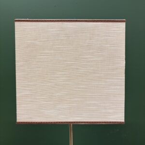 Paralume quadrato in tessuto beige chiaro con trama orizzontale e bordo intrecciato marrone scuro, su sfondo verde scuro.