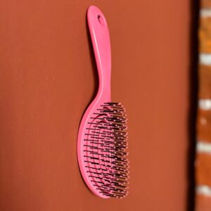 Spazzola districante ergonomica di colore rosa acceso con setole nere e punte rosa, appoggiata su sfondo marrone.