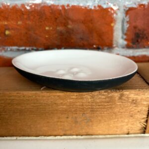 Portasapone ovale bicolore in ceramica con interno bianco e esterno nero, poggiato su una superficie di legno.