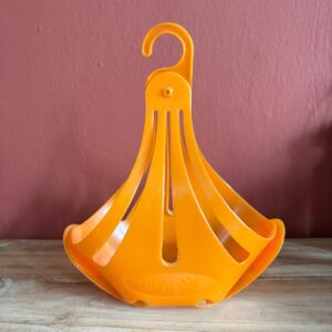 Cestino asciugabiancheria pieghevole in plastica arancione brillante con gancio, appoggiato su una superficie di legno.