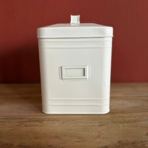 Contenitore rettangolare in metallo smaltato bianco crema con coperchio e porta etichetta frontale, su tavolo di legno.