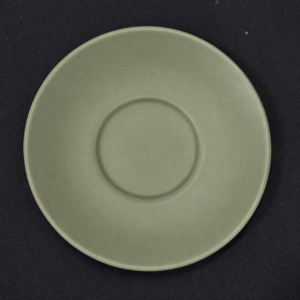 Piattino sottotazza rotondo di colore verde salvia opaco, con incavo centrale, su sfondo scuro.