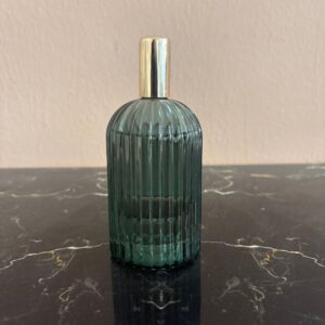 Flacone decorativo in vetro scanalato verde teal con tappo cilindrico dorato, posizionato su una superficie di marmo nero.