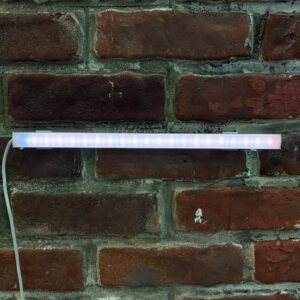 Barra LED lineare bianca con luce multicolore accesa, montata orizzontalmente su una parete di mattoni rossi.