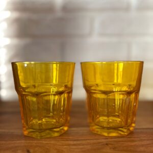Due bicchieri in vetro giallo ambra con design sfaccettato e base esagonale, posizionati su una superficie di legno.
