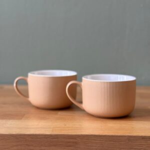 Due tazze in ceramica color pesca con superficie rigata e interno bianco, posizionate su un tavolo di legno.
