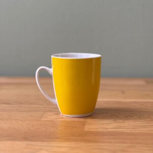 Tazza in ceramica di colore giallo brillante con interno e manico bianchi, posizionata su un tavolo di legno.