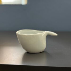 Lattiera in ceramica bianca opaca con beccuccio integrato, dal design moderno e minimalista, posizionata su una superficie scura.