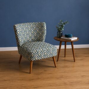 Poltrona accent con rivestimento in tessuto a motivo geometrico Art Déco verde, crema e oro, su gambe in legno, posta su pavimento in parquet davanti a parete blu.