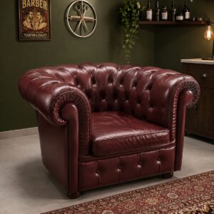 Poltrona Chesterfield singola in similpelle bordeaux con capitonnè e braccioli arrotolati, su pavimento chiaro con tappeto.