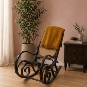 Sedia a dondolo vintage in legno scuro con schienale e seduta in paglia di Vienna, coperta da una coperta gialla, in un ambiente interno.