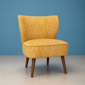 Poltroncina accent imbottita di colore giallo ocra con motivo a foglie bianche e gambe affusolate in legno scuro, su sfondo blu.