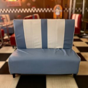 Panca da diner in stile anni '50 con schienale a strisce verticali blu chiaro e bianco, seduta blu, su pavimento a scacchi.