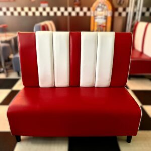 Divanetto imbottito rosso e bianco in stile diner americano anni '50, con schienale a strisce verticali, su pavimento a scacchi.