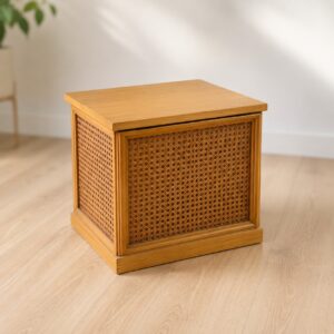 Cubo contenitore quadrato in legno chiaro con pannelli laterali in rattan intrecciato, posizionato su pavimento in parquet.