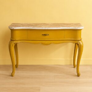 Consolle vintage gialla con finitura invecchiata, piano effetto marmo, un cassetto e gambe cabriole intagliate, su sfondo giallo.