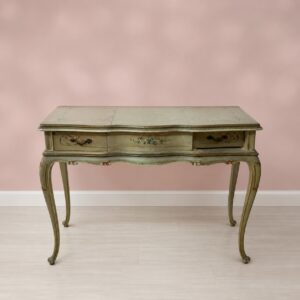 Consolle toeletta antica in legno laccato verde salvia con decorazioni floreali e gambe cabriole, su sfondo rosa.