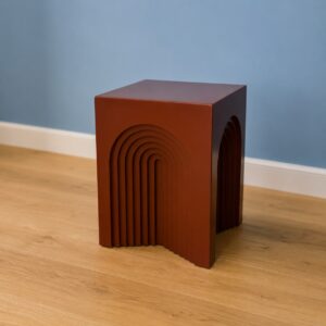 Sgabello decorativo color terracotta con design geometrico a forma di archi incassati, su pavimento in legno chiaro.