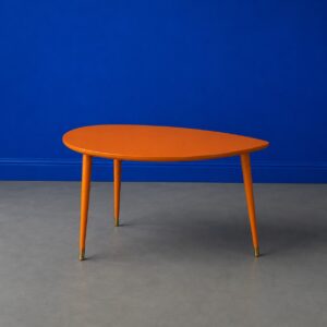 Tavolino da caffè arancione brillante con piano a forma organica e gambe affusolate con puntali in ottone, su sfondo blu.