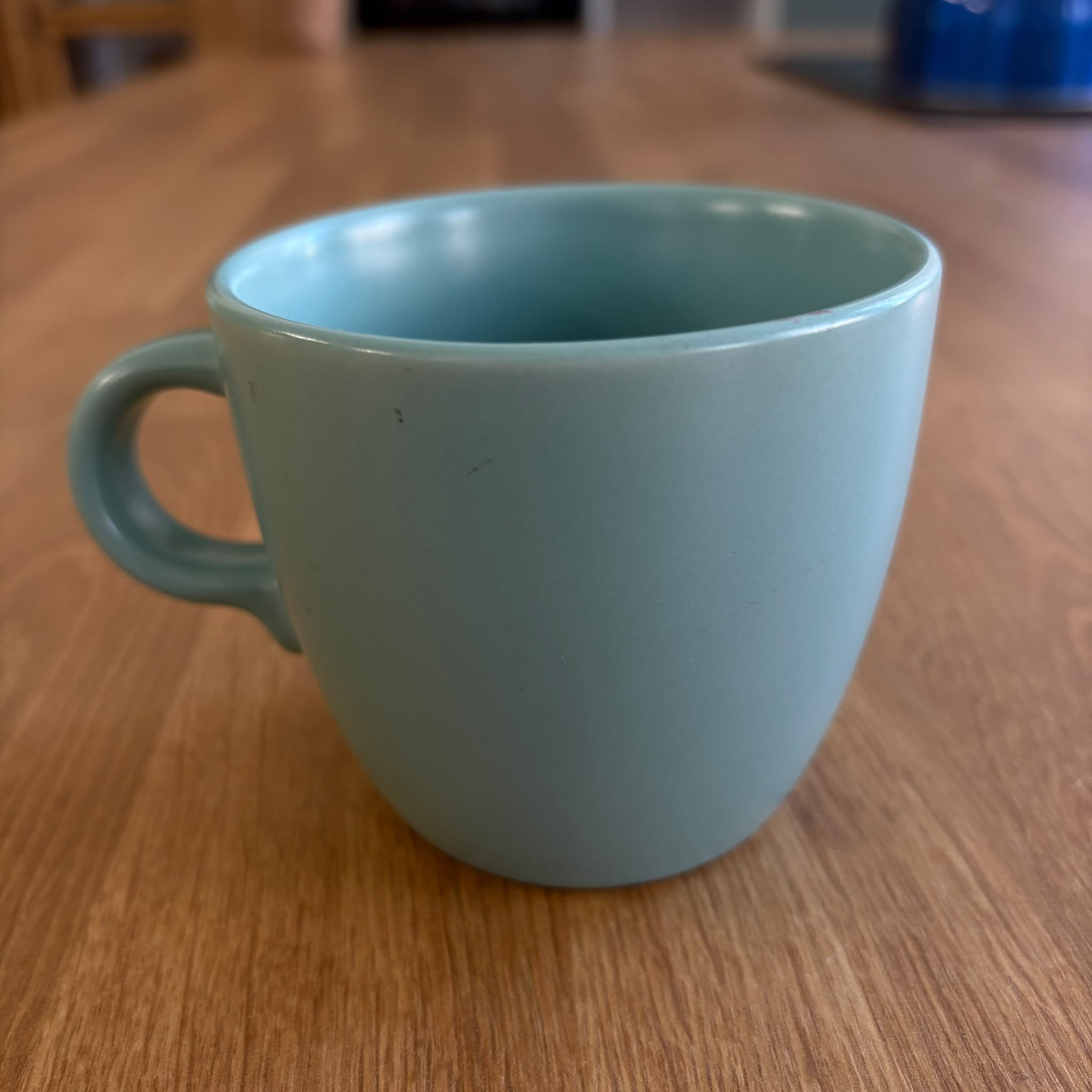 Tazza in ceramica di colore azzurro pastello con finitura opaca, posizionata su un tavolo di legno chiaro.