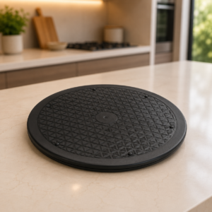Piatto girevole nero con superficie antiscivolo su un bancone da cucina chiaro, con sfondo sfocato di una cucina moderna.