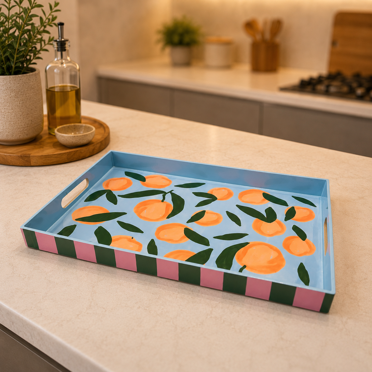 Vassoio rettangolare decorativo con motivo di arance e foglie su sfondo azzurro, bordi a strisce rosa e verdi, su un bancone da cucina.