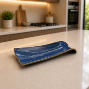 Vassoio ondulato in ceramica blu lucida con bordo dorato, posizionato su un piano di lavoro chiaro in una cucina moderna.