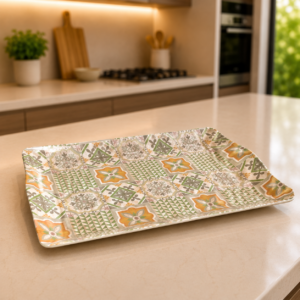 Vassoio rettangolare con fantasia a piastrelle geometriche e floreali nei toni del verde, arancione e grigio, su un bancone da cucina.