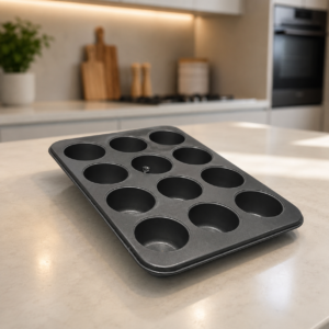Stampo antiaderente grigio scuro per 12 muffin, posizionato su un bancone da cucina chiaro in un ambiente moderno.