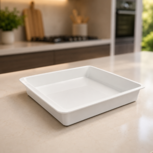 Teglia da forno rettangolare bianca in ceramica, posizionata su un piano di lavoro chiaro in una cucina moderna e sfocata.