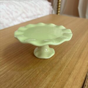 Alzatina decorativa in ceramica di colore verde menta con bordo ondulato, posizionata su una superficie di legno chiaro.