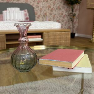 Vaso decorativo in vetro bicolore rosa e grigio fumé con bordo ondulato, affiancato da due libri antichi su un tavolino di vetro.