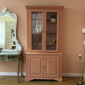 Credenza vetrina in legno dipinto di rosa pesca con ante superiori a vetro e ante inferiori a pannello, stile vintage.