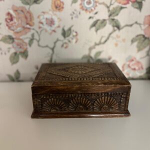 Scatola decorativa in legno scuro con intagli geometrici e a ventaglio sul coperchio e sui lati, posta su una superficie chiara.