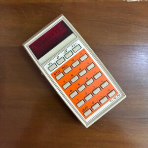 Calcolatrice vintage Texas Instruments TI-1270 con scocca beige, tastiera arancione e tasti grigi, display rosso, su sfondo di legno.